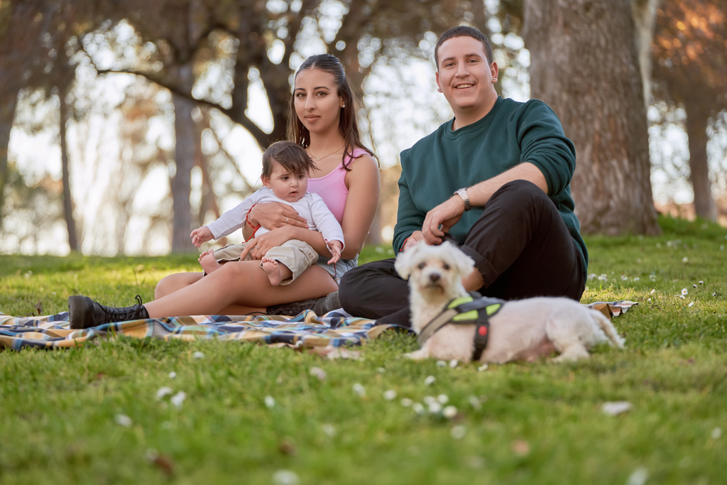 A young and cheerful family spending quality time on a beautiful summer day, sitting on the grass with their baby and dog.